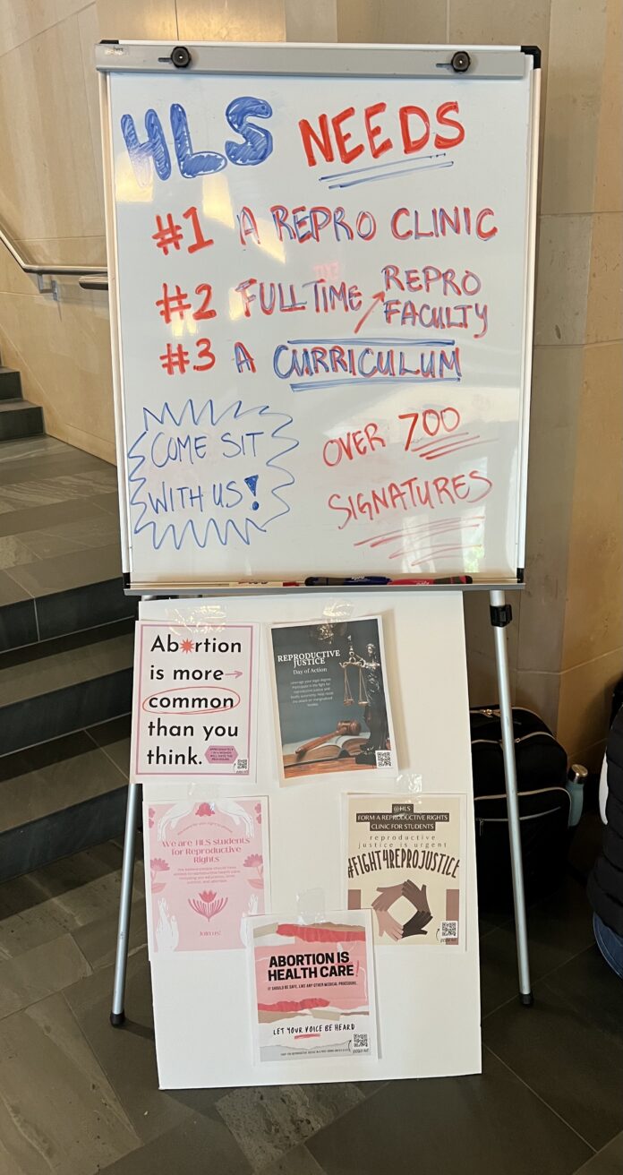 Whiteboard that says that HLS needs a repro clinic, full-time repro faculty, and a repro curriculum. The whiteboard also has messages asking students to come sit and mentioning that the letter has over 700 signatures.