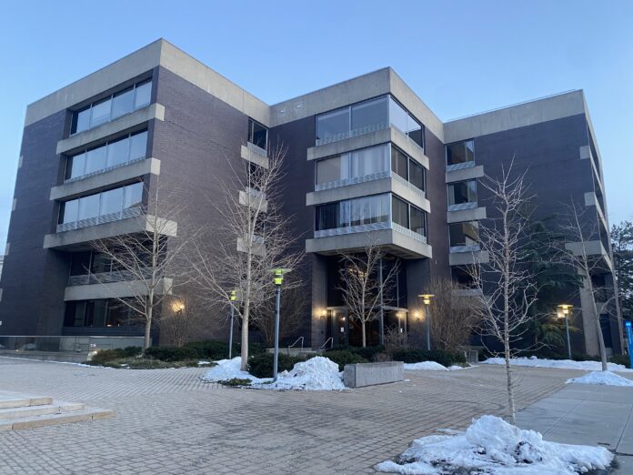 View of Pound Hall. Snow is on the ground, but walkways are clear, and the leaves have fallen off the trees. Streetlights outside are alight.
