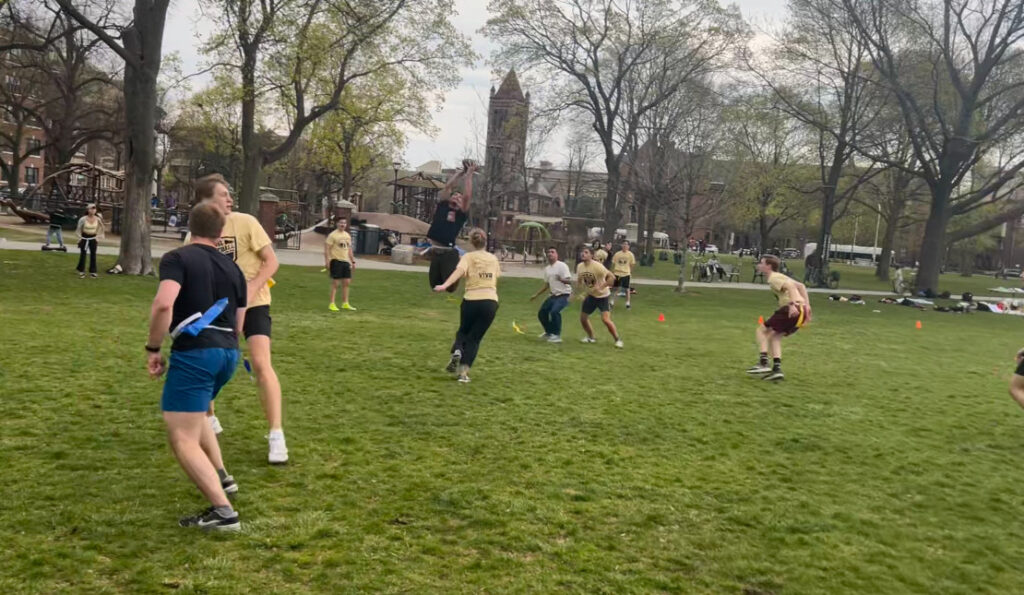 Several flag football players running in Cambridge Common park in the midst of a match.